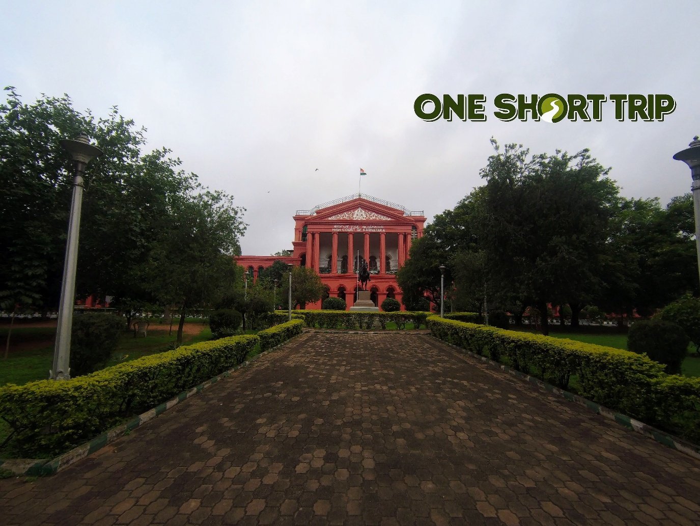 Tree-lined avenue leading to the red facade of the High Court of Karnataka